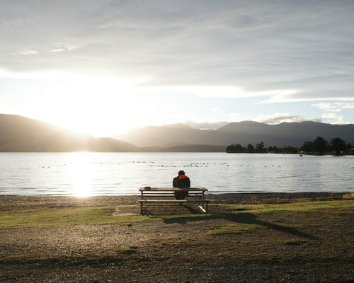person sitting by a calm lake at sunrise focusing on deep breathing exercises